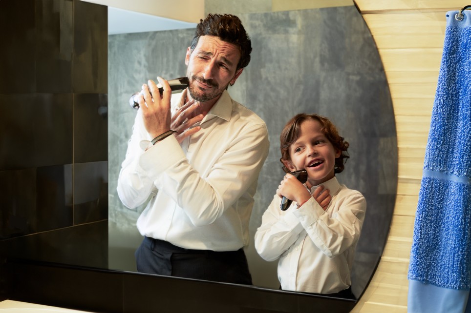Vater und sein Sohn im Kindesalter stehen im Hemd vor einem Spiegel und rasieren sich im Gesicht Vater und sein Sohn im Kindesalter stehen im Hemd vor einem Spiegel und rasieren sich im Gesicht