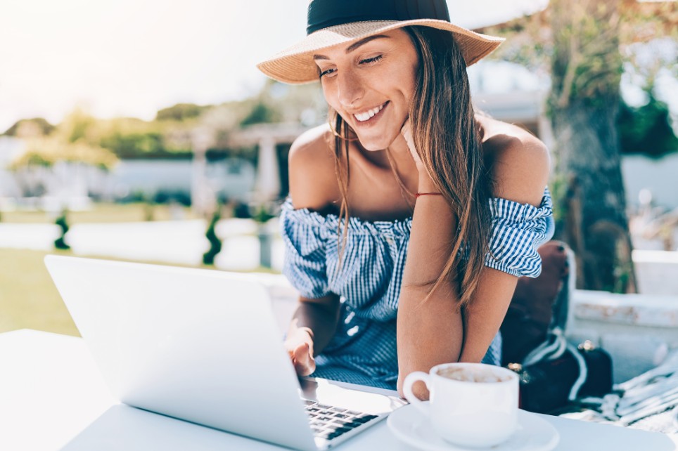 Eine junge Frau sitzt mit ihrem Laptop und einem Kaffee in der Sonne Eine junge Frau sitzt mit ihrem Laptop und einem Kaffee in der Sonne