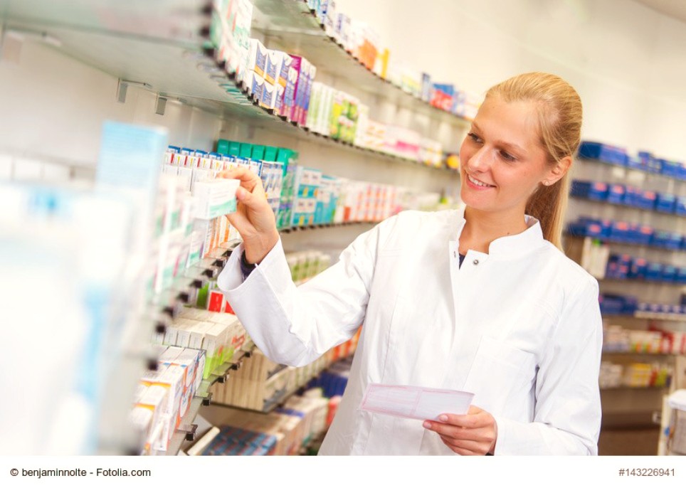 Eine junge Apothekerin hält ein Rezept in der Hand und greift gleichzeitig nach einem Medikament im Regal Eine junge Apothekerin hält ein Rezept in der Hand und greift gleichzeitig nach einem Medikament im Regal