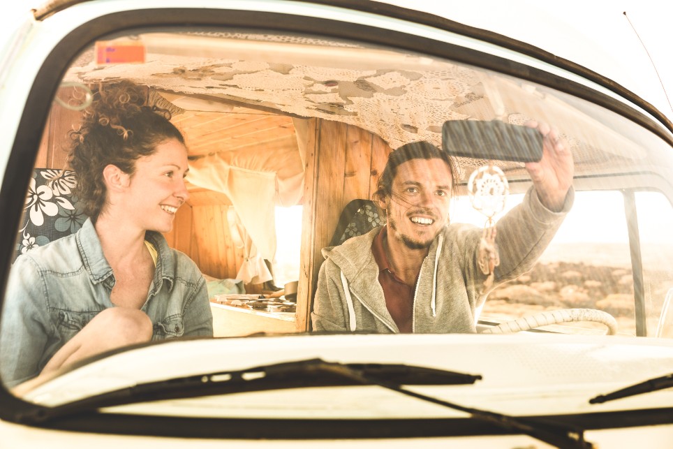 Eine junge Frau und ein junger Mann sitzen zusammen auf den Vordersitzen eines Campervans Eine junge Frau und ein junger Mann sitzen zusammen auf den Vordersitzen eines Campervans