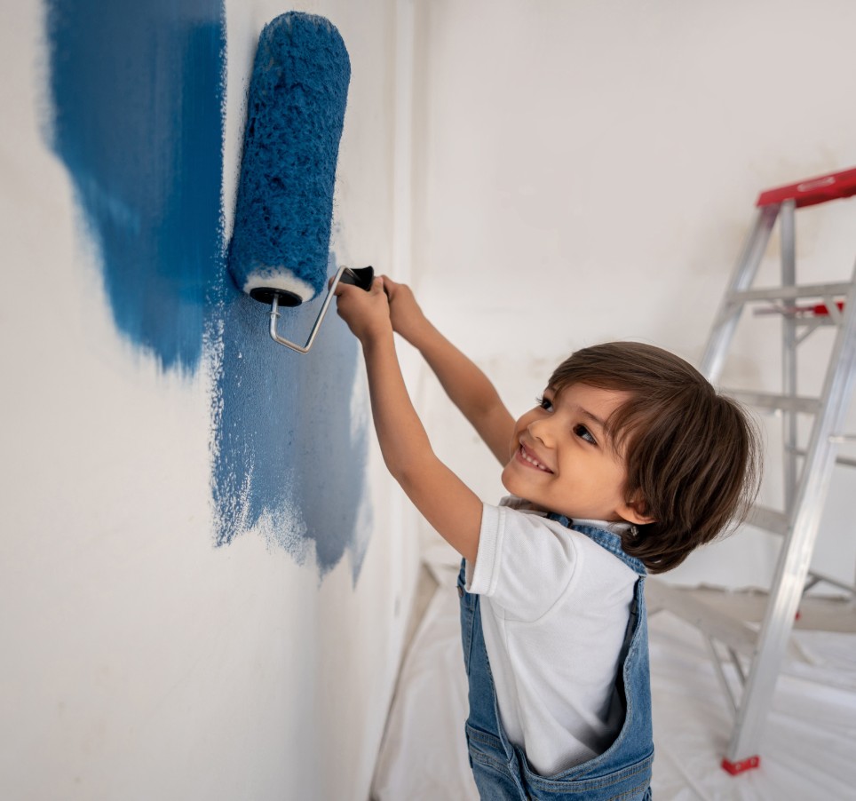 Ein kleiner Junge malt eine Wand mit blauer Farbe an.