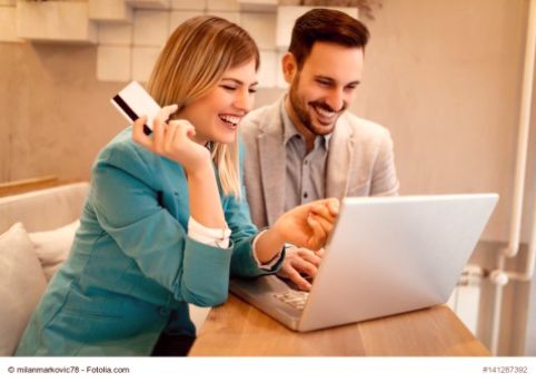 Eine Frau, die eine Kreditkarte in der rechten Hand hält, und ein Mann sitzen lächelnd zusammen vor einem Laptop 