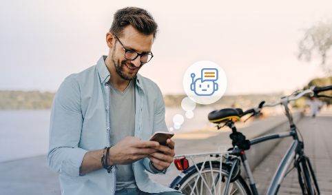 Mann sitzt neben seinem Fahrrad und nutzt auf seinem Handy den Chatbot