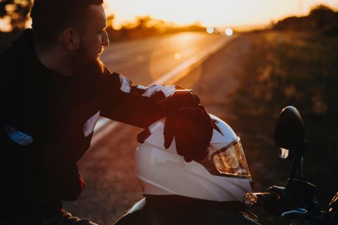 Motorradfahrer macht während einer Fahrt bei Sonnenuntergang eine Pause. Der Helm liegt auf dem Motorrad.