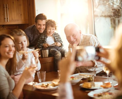 Kinder mit ihren Eltern und Großeltern sitzen gemeinsam zuhause am Esstisch.