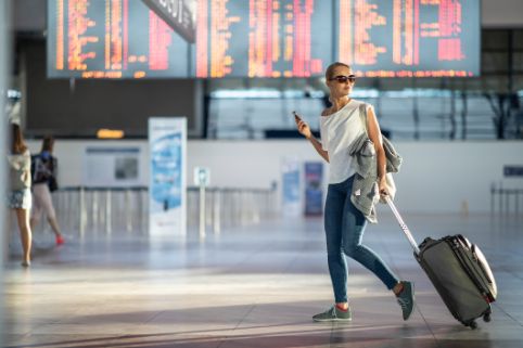 Eine junge Frau läuft mit ihrem Handgepäckskoffer durch die Eingangshalle eines Flughafens