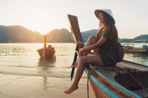 Eine junge Frau sitzt auf dem Rand eines Boots in der Sonne am Strand