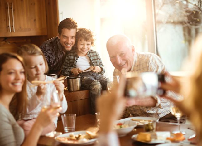 Kinder mit ihren Eltern und Großeltern sitzen gemeinsam zuhause am Esstisch.