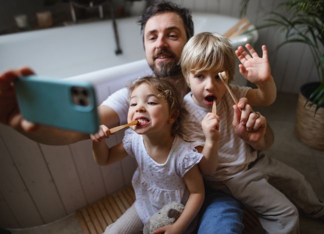 Ein Vater nimmt mit seiner Tochter und seinem Sohn ein Selfie auf, während sie beide am Zähne putzen sind.