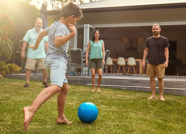 Ein kleiner Junge tritt gegen einen blauen Ball, beobachtet von zwei Männern und einer Frau.