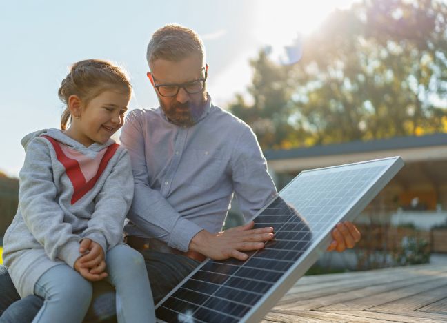Vater zeigt seiner kleinen Tochter ein Solarpaneel für eine Photovoltaik-Anlage